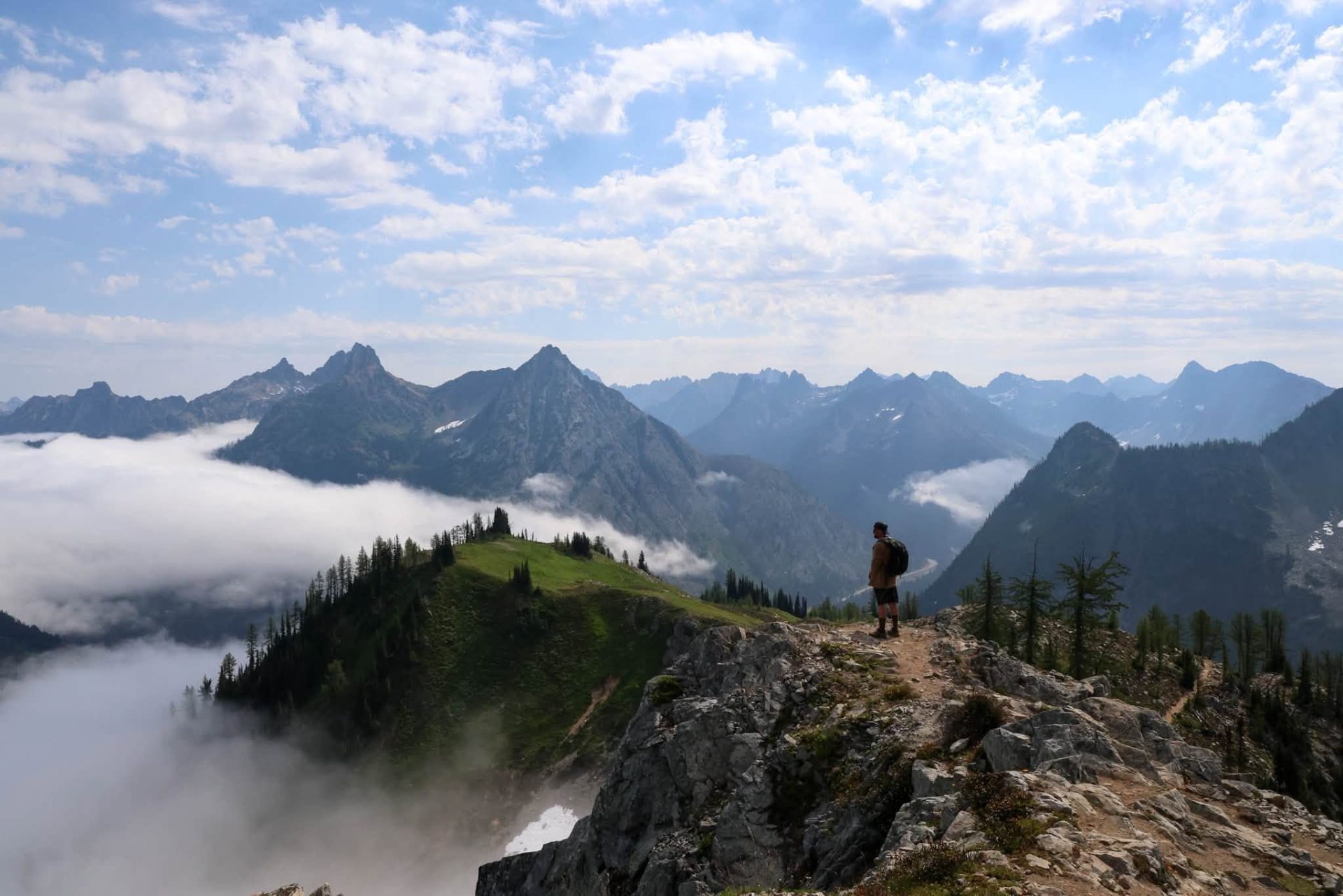A hiker standing on a rocky mountain ridge above a sea of clouds